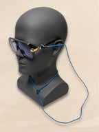 A pair of black sunglasses with gold temple details and a blue SpecTether attached, 