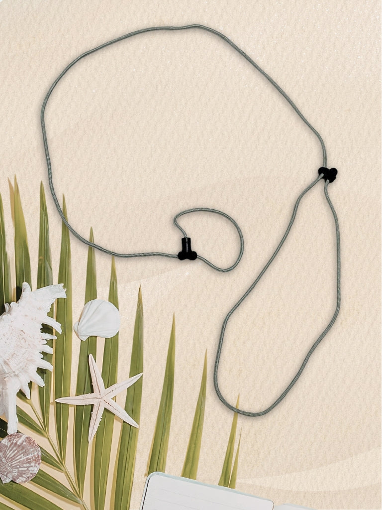 A gray cord SpecTether with black plastic clasps, laid out on a textured beige background with decorative palm leaves, seashells, and a starfish.