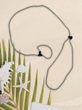 A gray cord SpecTether with black plastic clasps, laid out on a textured beige background with decorative palm leaves, seashells, and a starfish.