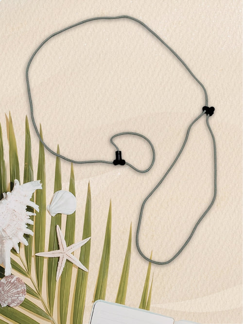 A gray cord SpecTether with black plastic clasps, laid out on a textured beige background with decorative palm leaves, seashells, and a starfish.
